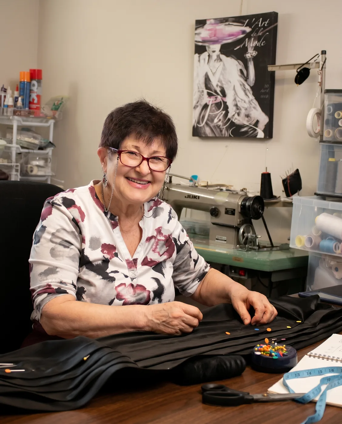 Designer Rita Kleiner smiling at her studio worktable while hand-finishing a garment